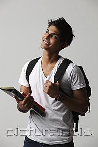 PictureIndia - young man looking up, wearing back pack and holding books.
