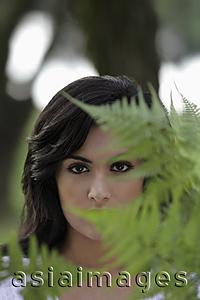 Asia Images Group - Head shot of young woman looking through ferns