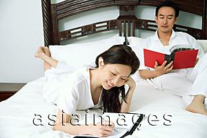 Asia Images Group - Couple in bedroom, woman writing in diary, man reading book