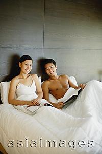 Asia Images Group - Couple sitting up in bed, with book and magazine, smiling at camera