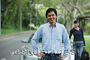 Asia Images Group - Man with hands on hips, standing in front of car, woman in the background with luggage