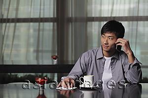 Asia Images Group - Young man sitting at a table talking on the phone