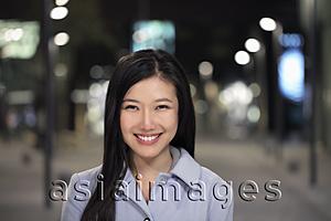 Asia Images Group - Head shot of young woman smiling on the street at night