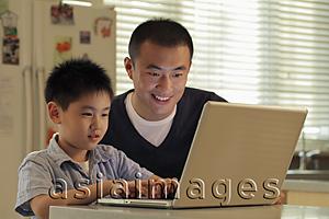 Asia Images Group - Father and son working on laptop computer together in kitchen