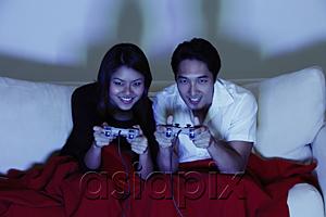 AsiaPix - Couple sitting side by side on sofa, playing with video games