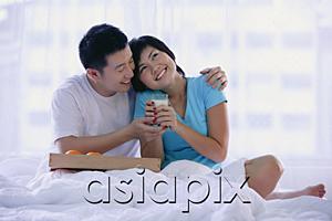 AsiaPix - Couple sitting on bed, woman holding glass of milk