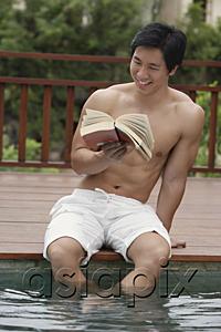 AsiaPix - Man sitting at the edge of swimming pool, reading a book
