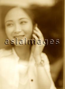 Asia Images Group - Young woman standing behind window, talking on cellular phone