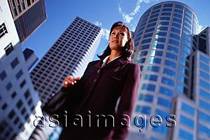 Asia Images Group - Female executive standing in front of high-rise buildings, low angle view