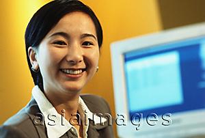 Asia Images Group - Female executive smiling with computer monitor in background