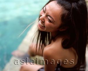 Asia Images Group - Woman sitting by side of swimming pool, laughing