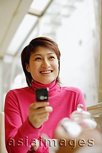 Asia Images Group - Young woman holding mobile phone, facing another person