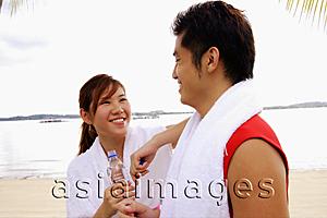 Asia Images Group - Couple standing at beach, side by side, holding water bottles, smiling