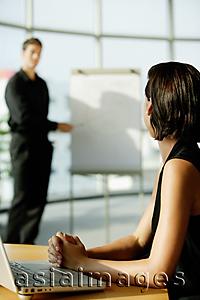 Asia Images Group - Female executive sitting at desk, looking at colleague standing next to flip board