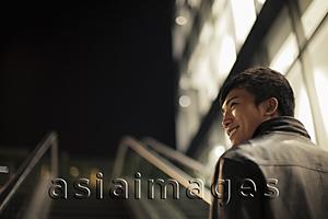 Asia Images Group - Rear view of young man going up an escalator at night