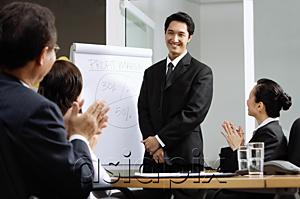 AsiaPix - Businessman standing next to flipchart, other executives clapping