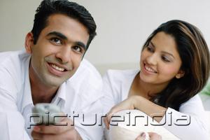 PictureIndia - Couple side by side, man holding TV remote control, woman looking at him